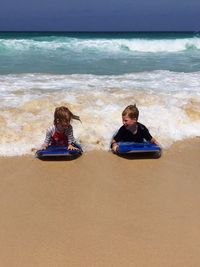Happy siblings lying with surfboards on shore at beach during sunny day