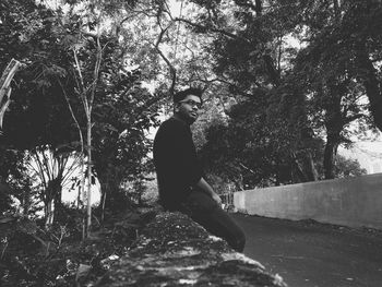 Portrait of young man sitting on tree in forest