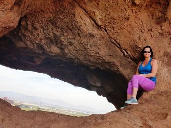 Smiling woman in sunglasses sitting on rock