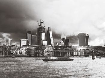 Modern buildings by river against sky in city