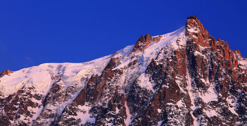 Low angle view of snowcapped mountains against clear blue sky