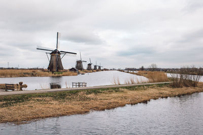 Traditional windmill by canal against sky