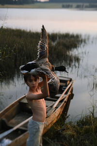 Side view of boy holding bird against sky