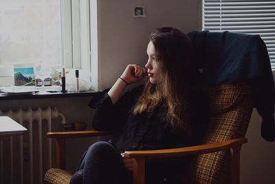 Thoughtful young woman looking away while sitting on chair at home