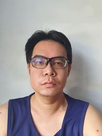 Portrait of young man wearing eyeglasses against wall