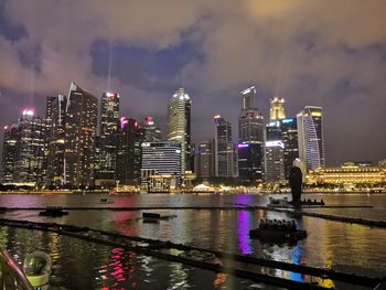 Illuminated buildings by river against sky at night