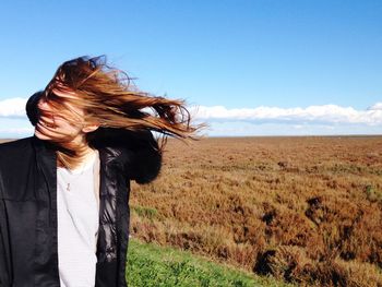 Smiling woman with tousled hair standing on field against sky