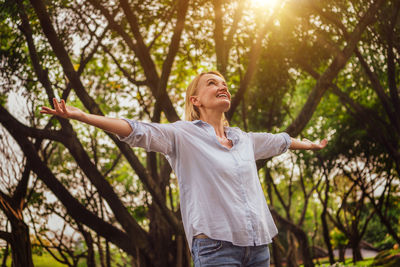 Young woman with arms outstretched standing against trees