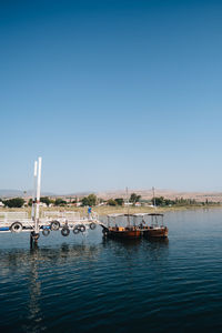 Boats in lake against clear blue sky