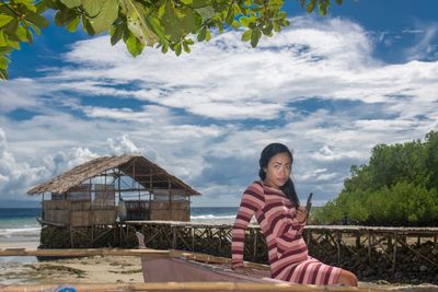 Portrait of woman sitting at beach against sky