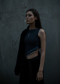 Young woman looking away while smoking standing against wall