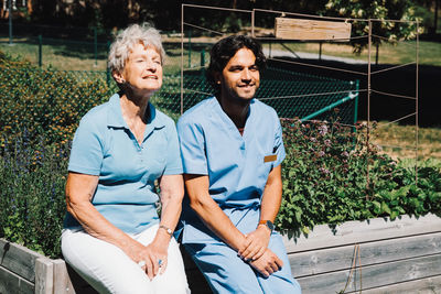 Smiling senior woman sitting with male nurse on planter at back yard