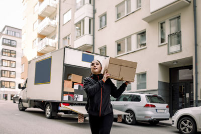 Young delivery woman carrying box on street