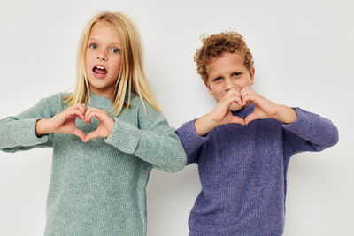 Portrait of sibling making heart shape against white background