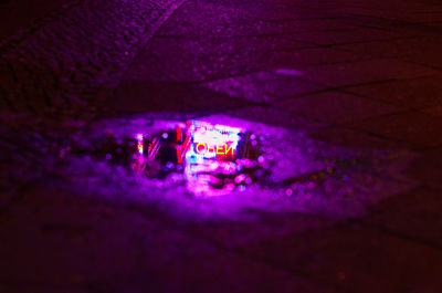 Illuminated open sign reflecting in puddle at night