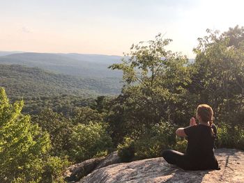 Woman meditating on cliff against mountains during sunset