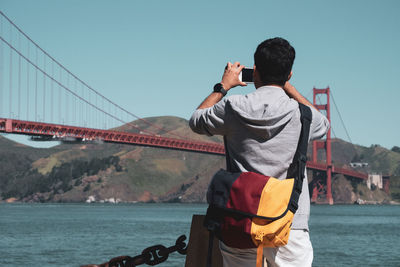 Rear view of man standing on bridge over sea against sky