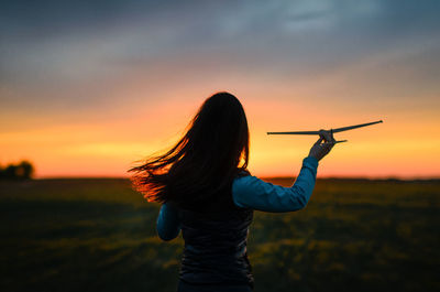 Rear view of woman standing against sky during sunset