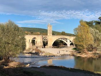 Arch bridge over river by building against sky