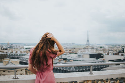 Rear view of young woman standing by railing in city