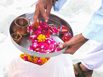 Low section of man holding plate with flowers and diya