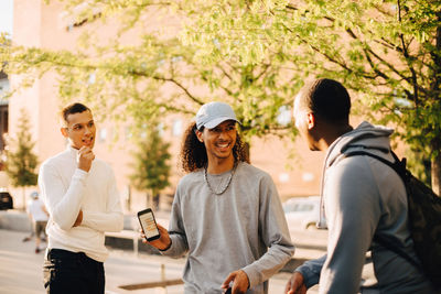 Smiling man showing smart phone to friends at skateboard park