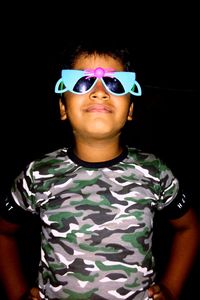 Portrait of young man wearing sunglasses standing against black background