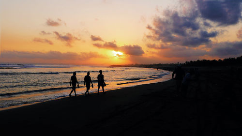 Silhouette people on beach against sky during sunset