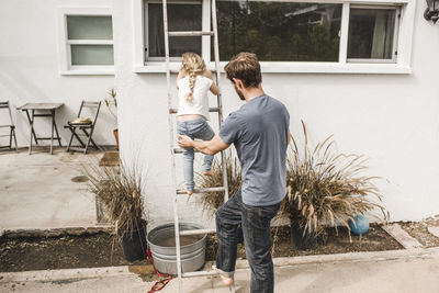 Rear view of father assisting daughter to climbing ladder at house