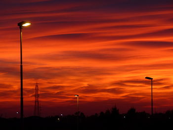 Low angle view of silhouette street lights against orange sky