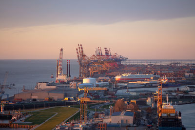 Cranes at commercial dock against sky during sunset