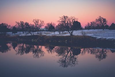 Reflection of silhouette trees in lake against sky during sunset