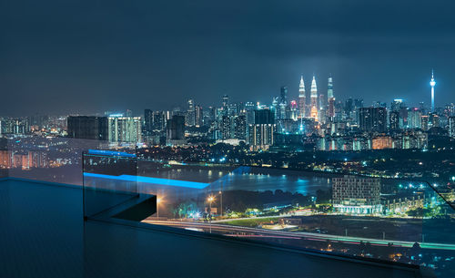 Illuminated modern buildings in city against sky at night