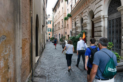 Rear view of people walking on footpath amidst buildings in city