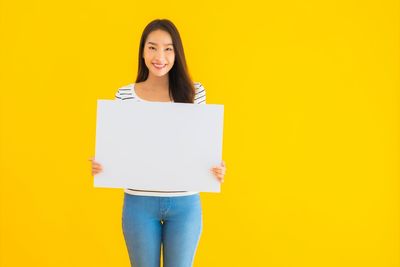 Portrait of smiling woman standing against yellow background