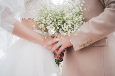 Midsection of bride and bridegroom holding bouquet