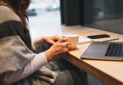 Midsection of woman using mobile phone while sitting on table