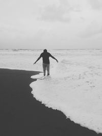 Rear view of man standing on beach against sky