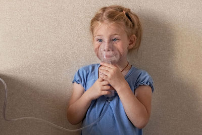 Little girl makes inhalation with a nebulizer at home, sitting on a chair. 