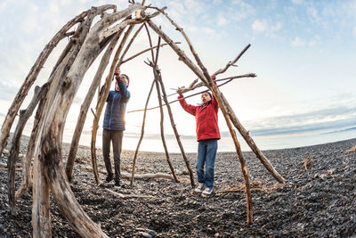 Two brothers building a hut out of driftwood on a rocky beach