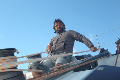 Man pulling rope on sailboat against blue sky