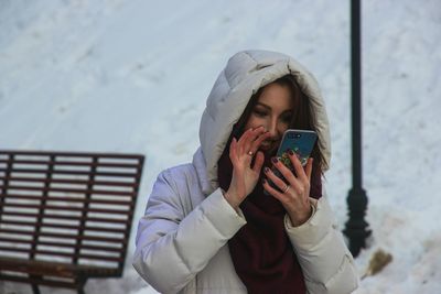 Young woman using mobile phone while standing on snow