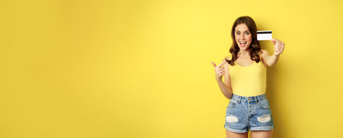 Young woman standing against yellow background