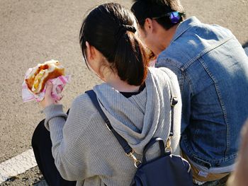 Rear view of man and woman eating burger while sitting outdoors