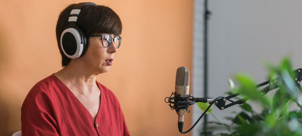 Portrait of young woman with microphone against wall