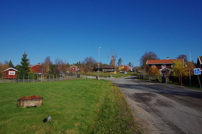 Street amidst field and houses against clear blue sky