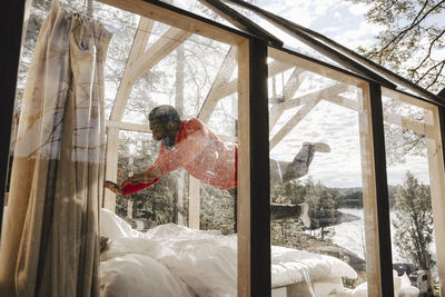 Cheerful man jumping on bed in glass cottage