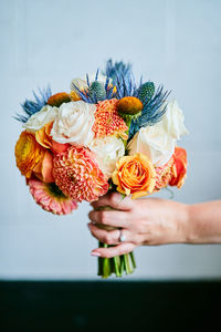 Cropped hand of woman holding bouquet against wall