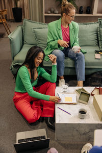 High angle view of smiling business professional writing in book while sitting near female colleague at office