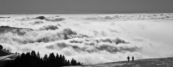 Silhouette people standing on mountain over cloudscape